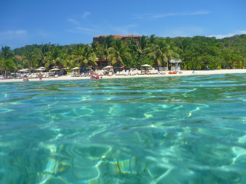 West Bay Beach seen from the sea, with its turquoise shiny waters giving way to a powdery white stretch of sand and thick forest in the distance