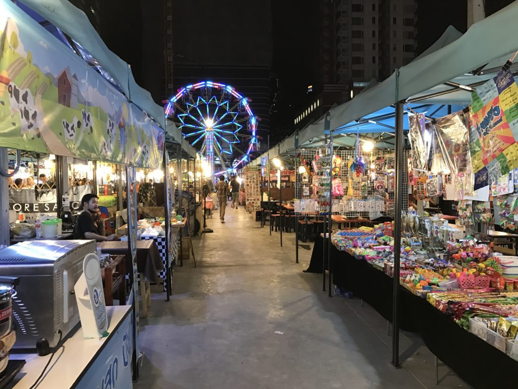 View of vendor stalls and the ferris wheel at Talad Neon Night Market in Thailand