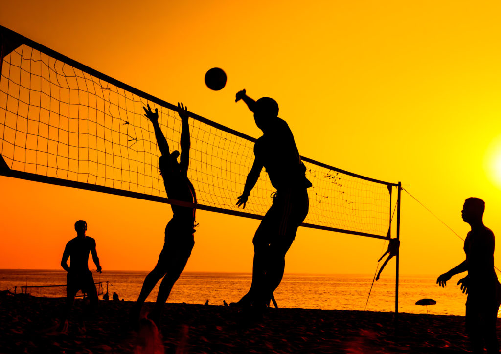 People playing volleyball at sunset on a beach with friends