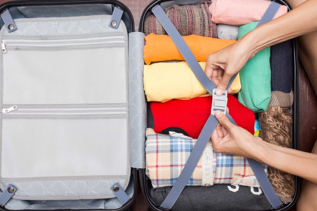 Person closing their suitcase with all their clothes inside