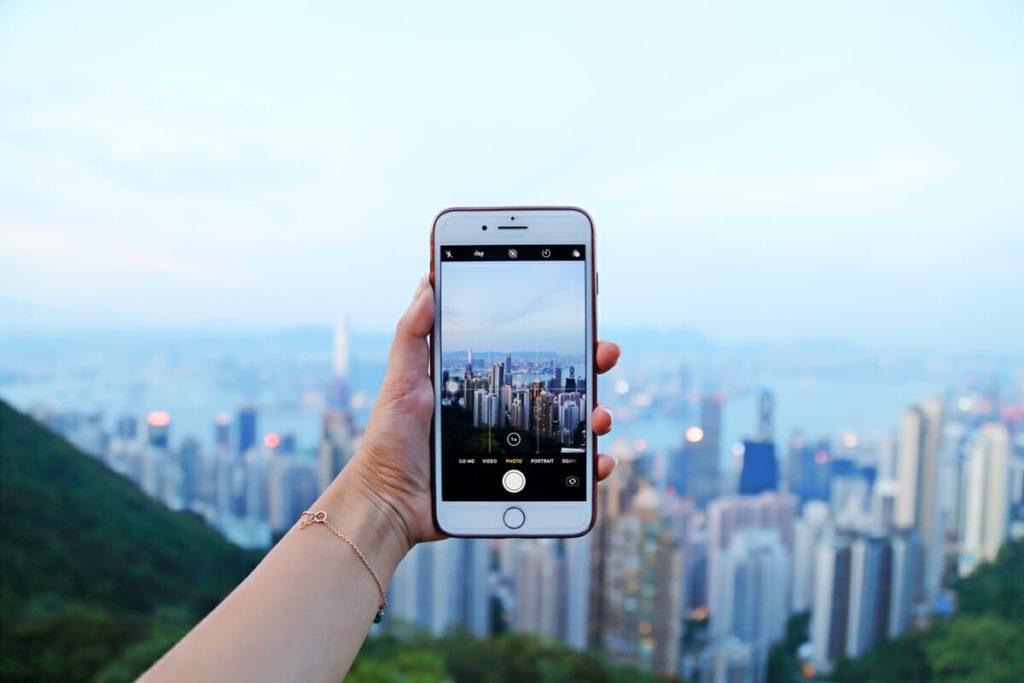 A person holds up an iPhone to take a picture of the skyline of a city at dusk