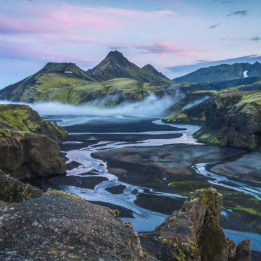 Mountains covered in green and brown with a water stream slowing toward the camera make for the best time to visit Iceland