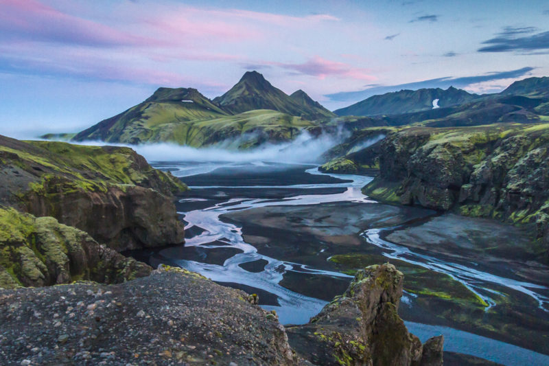 Mountains covered in green and brown with a water stream slowing toward the camera make for the best time to visit Iceland