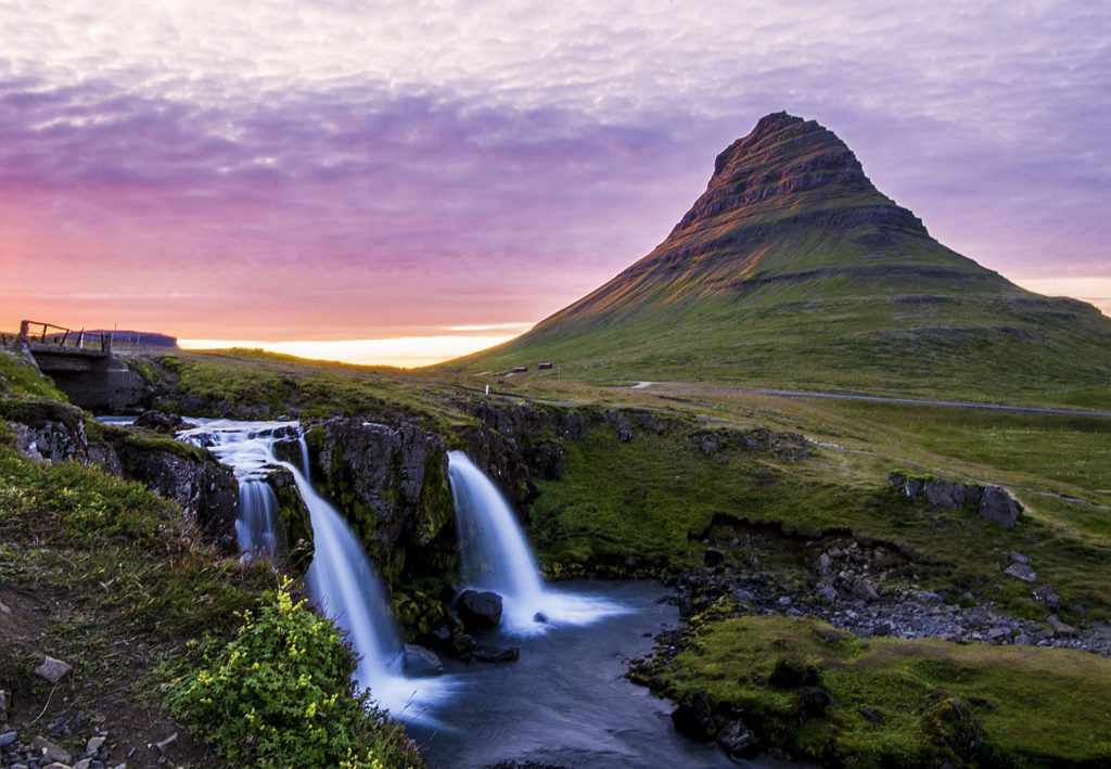The Kirkjufell mountain covered in green with a cascading waterfall at sunset