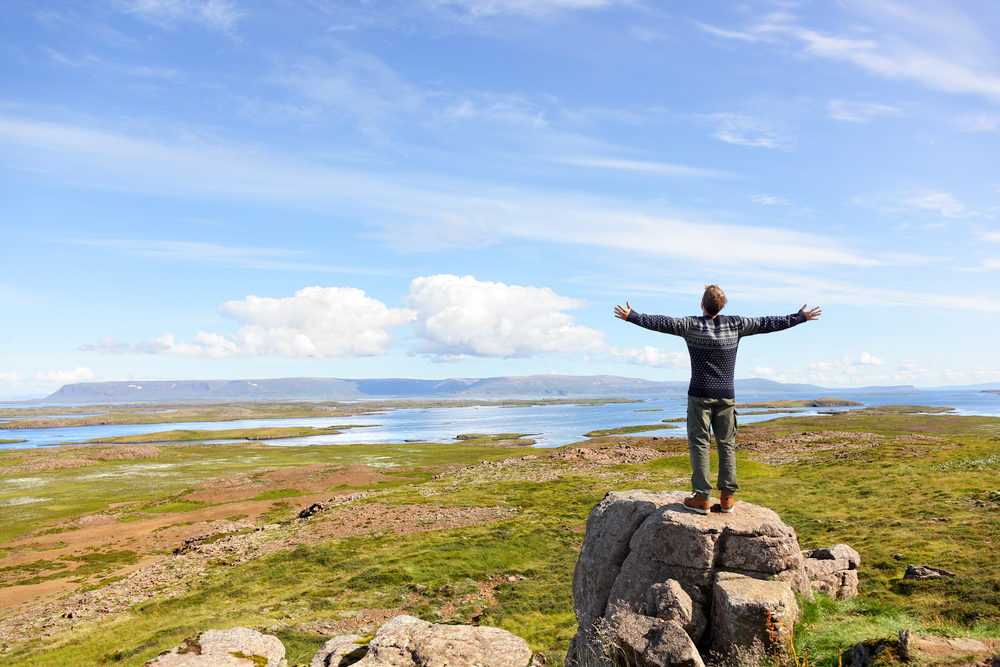 A man stands on a rock with his arms open taking in the fresh air of Iceland