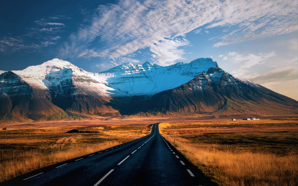 Open road in Iceland leading to snow-topped mountains and surrounded by dry vegetation